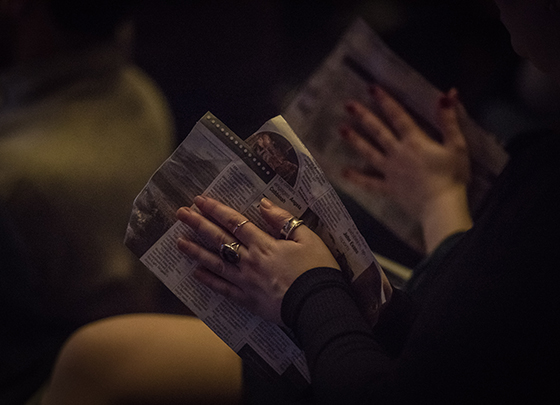 An audience member's hands rubbing two sheets of newspaper together
